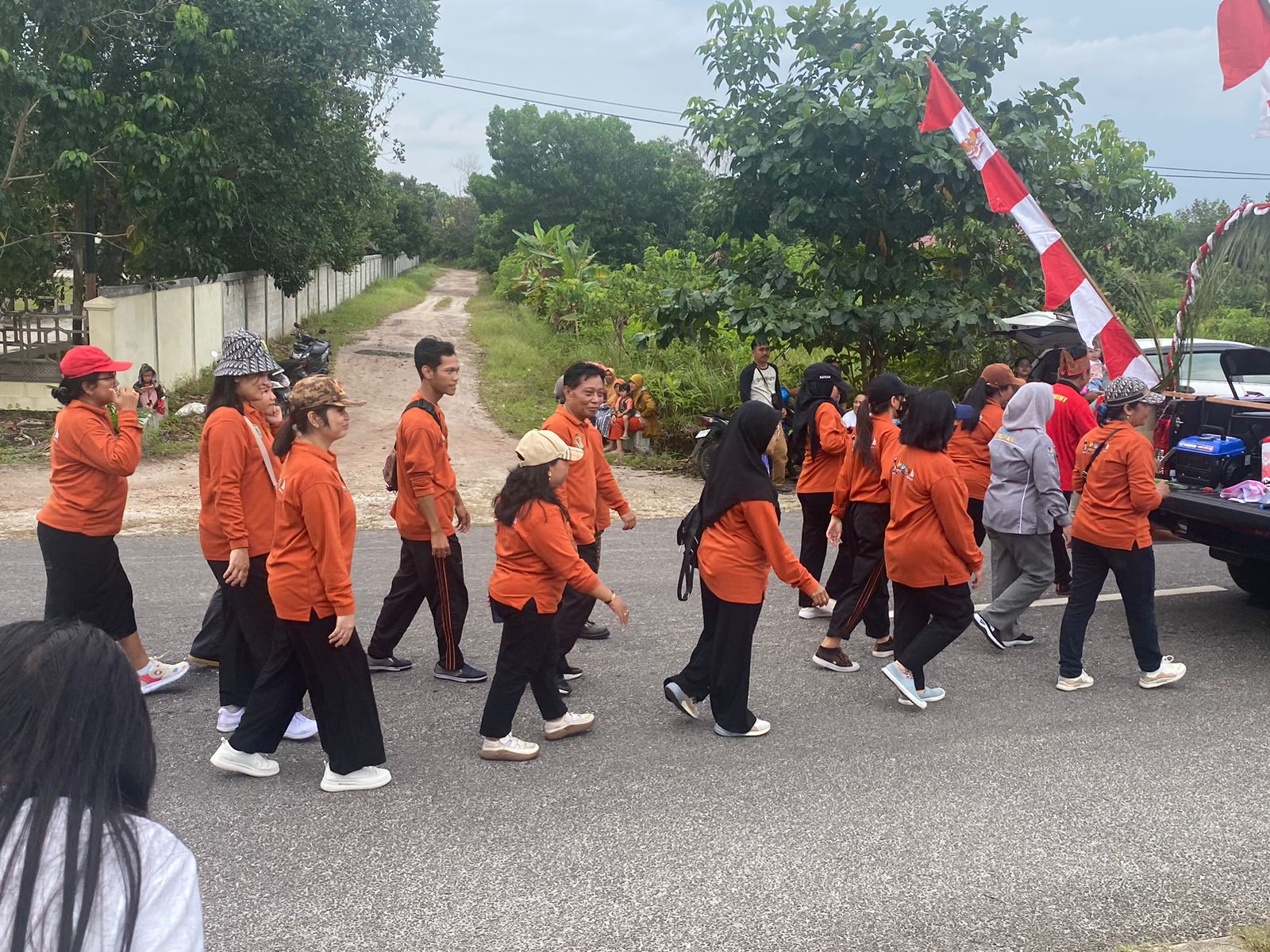 Pegawai dukcapil dengan seragam orangenya berjalan bersama dalam pawai budaya, memperlihatkan semang